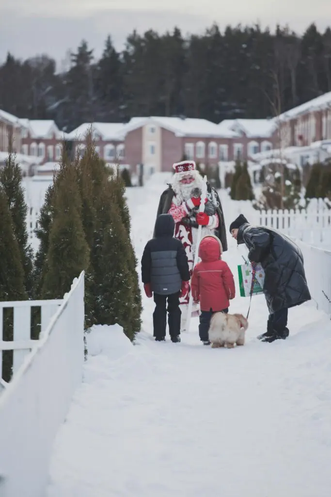 Children meeting Santa Claus outdoors in a snowy town with gifts and a cute dog.