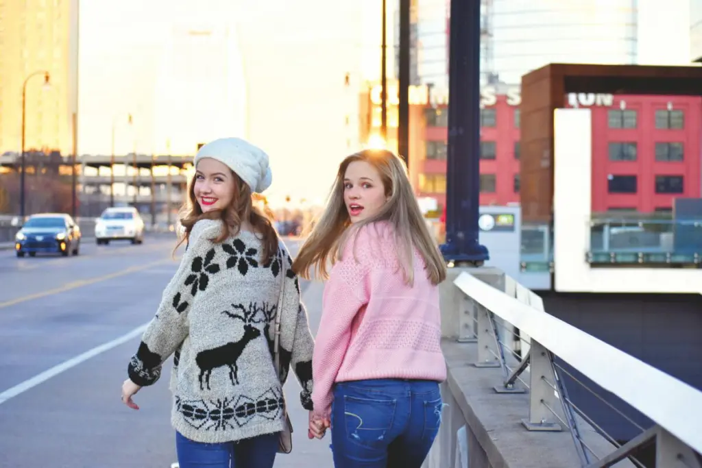 Two teenage friends holding hands on a sunny day in Nashville, wearing cozy sweaters.