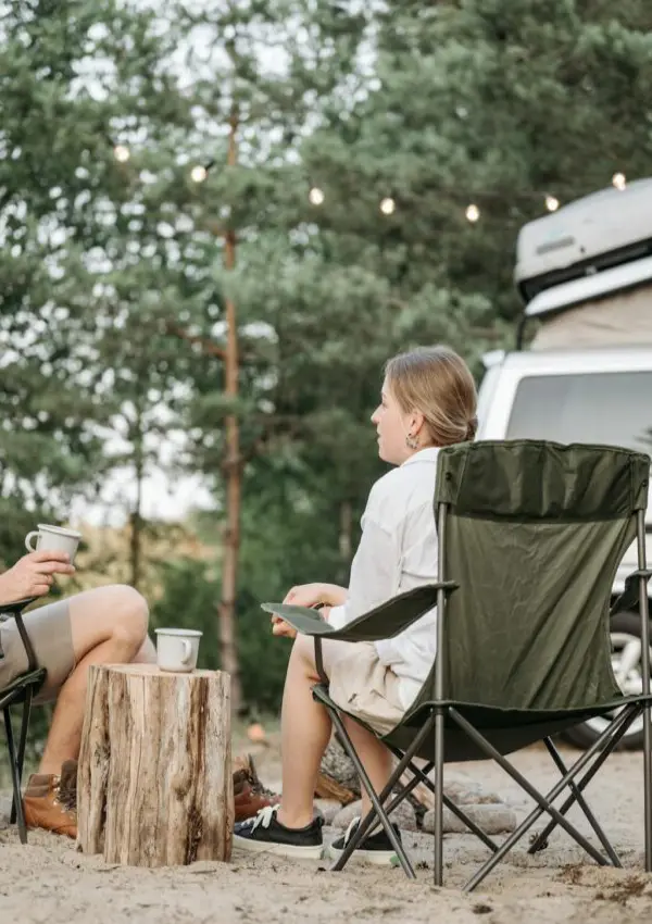 A couple enjoying a relaxed moment with coffee during a camping trip in nature by their camper van.